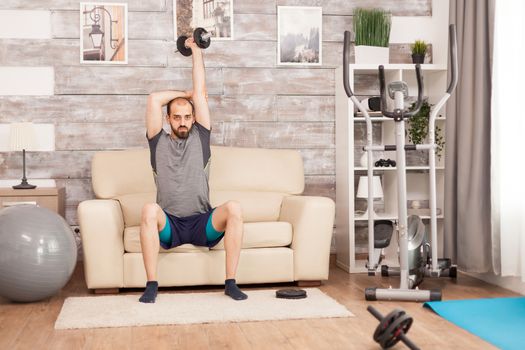 Athletic man increase his triceps strength using dumbbell during global self isolation.