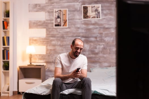 Man in comfortable pajamas at night laughing while watching a tv show.