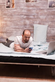 Man laying in bed in wearing pajamas using smartphone.