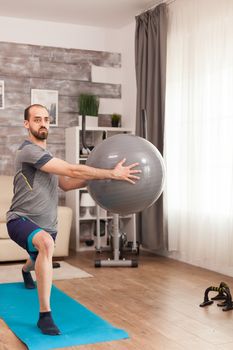 Athletic man doing lunges workout with swiss ball during self isolation.