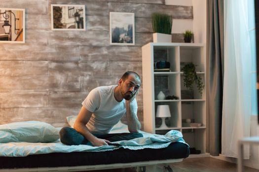 Sleepy man watching tv sitting on comfortable bed.