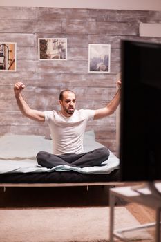 Cheerful man with hands raised watching sports on tv at night.