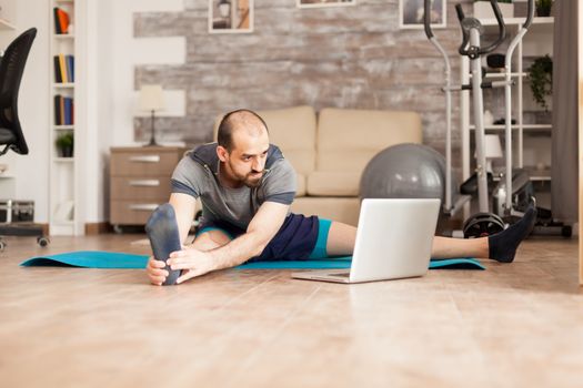 Man learning how to stretch his body looking at online course on laptop during coronavirus lockdown.