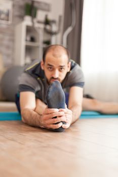 Man in sportswear stretching his legs on yoga mat during global pandemic.