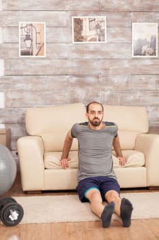 Fit man using sofa to train triceps during coronavirus lockdown.
