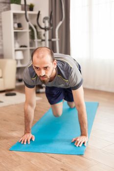 Fit man in his apartment doing mountain climbers exercise on yoga mat during global pandemic.
