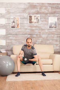 Strong man using dumbbells to trains his biceps at home during global pandemic.