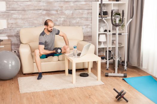 Fit man training his biceps with dumbbell watching online training during global pandemic.