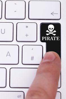 Finger pressing the pirate button and skull on keyboard. Illegall data transfer