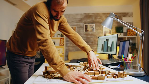 Successful architect talking on the phone while building a city model in his home office.
