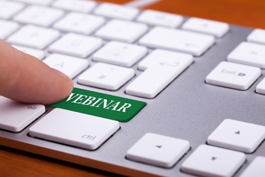 Green button on keyboard with webinar word on it. Finger pressing the button