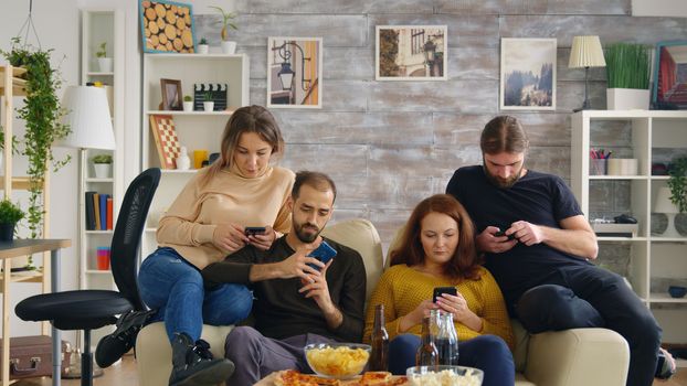 Young man taking a sip of beer while using his smartphone. Friends browsing on mobile phone.