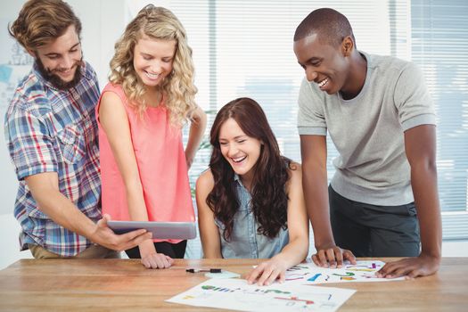 Happy man showing digital tablet to coworkers at desk