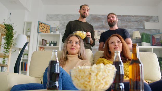 Girl pranking her friends with pizza in living room while their are watching a football match on tv.