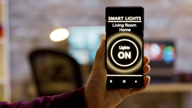 Close up shot of man holding a smartphone in hands with a smart light application on it