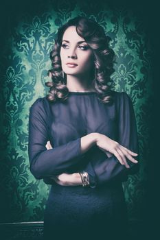 Elegant woman on vintage wall with green pattern. Professional make up and hairstyle. Old type camera toning
