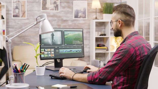 Creative filmmaker working on post production of a movie while working from home. Girlfriend in the background is walking in the house and talking on the phone.