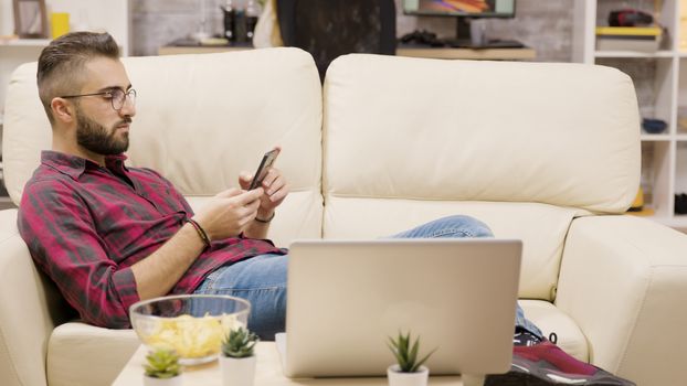 Handsome young man relaxing on couch using his phone. Girlfriend in the background.