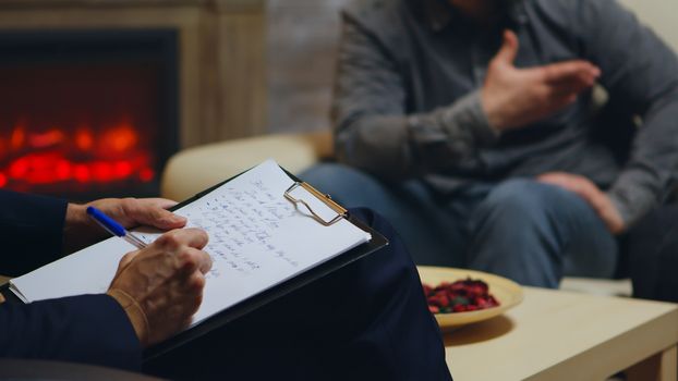 Close up of psychologist writing notes while couple yelling at relationship guidance.