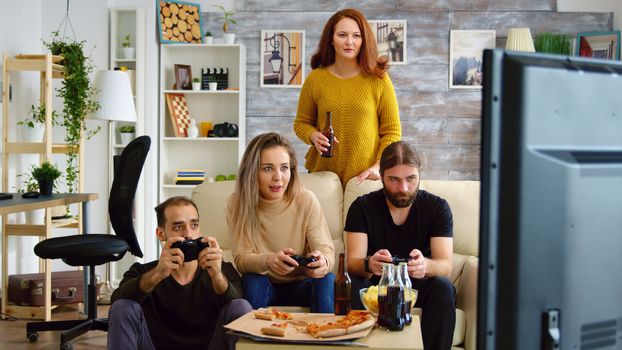 Cheerful caucasian friends playing video games on big tv in living room.
