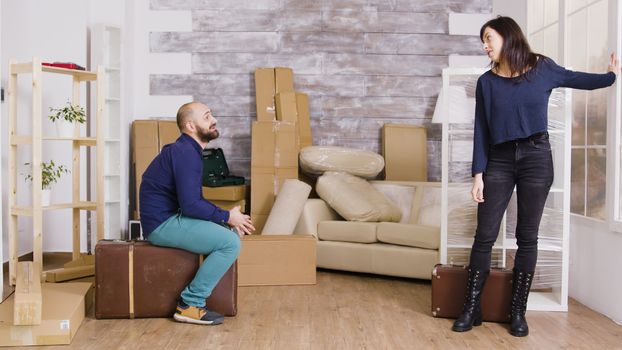 Happy caucasian couple carrying suitcases in their new apartment. Cardboard boxes in the background.