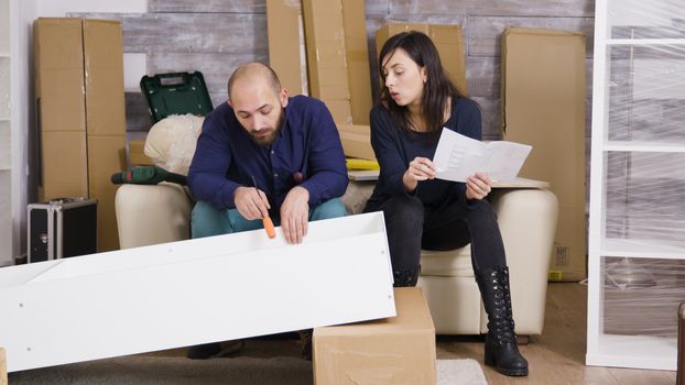 Young couple assembling a shelf as a team in their new apartment and reading instructions.