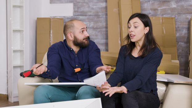 Angry girlfriend hitting boyfriend with furniture instructions. Couple assembling furniture in new apartment.