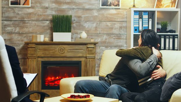 Young couple hug each other sitting on couch at therapy after talking about their difficulties.