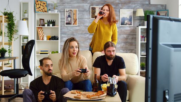 Cheerful caucasian friends playing video games on big tv in living room.