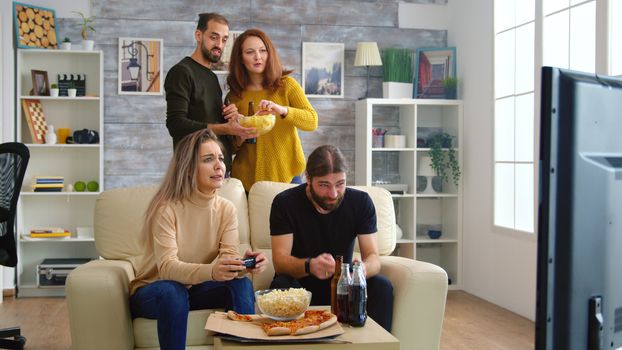 Cheerful caucasian friends playing video games on big tv in living room.