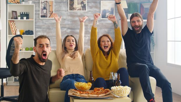 Group of friends happy after their favorite football team wins the championship. Friends sitting on sofa eating pizza and chips.