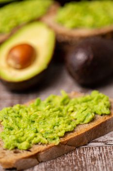 Avocado sandwiches next to cutted ones on wooden board.