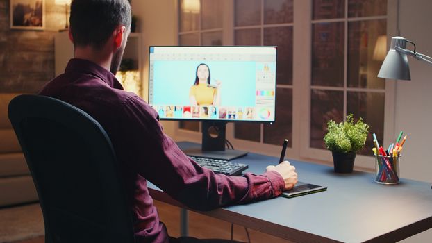 Male photographer editing photos in office at night time using graphic tablet.