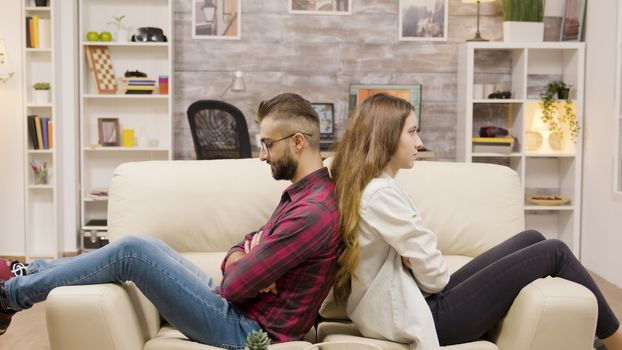 Couple sitting back to back on the couch with arms crossed. Distant couple.