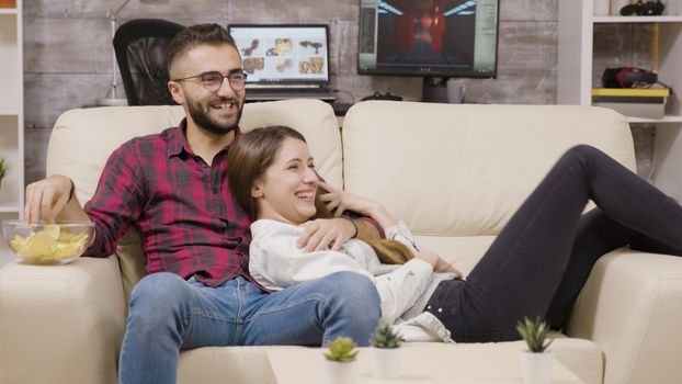 Couple sitting on the couch and laughing while watching tv.