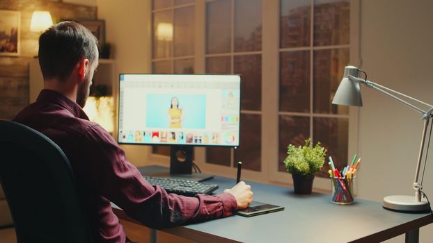 Professional photographer sitting at his desk retouching photos during night time using graphic tablet.