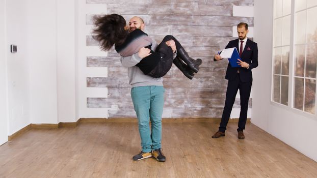 Boyfriend spining girlfriend after buying new apartment. Real estate agent signing documents in the background.
