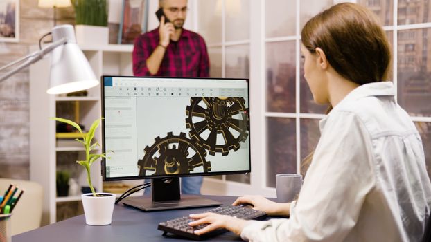 Female engineer working on a 3d design from home. Boyfriend in the background walks in the room and talks on the phone.