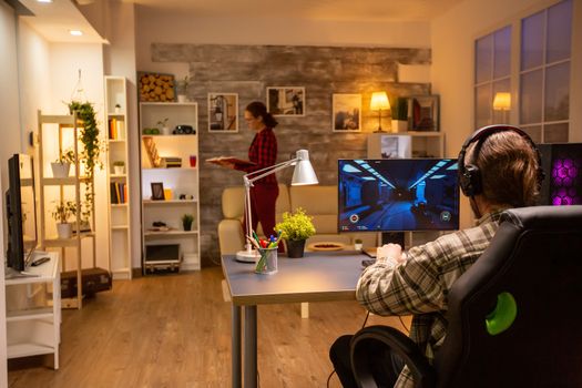 Back view of professional video gamer playing on powerful PC late at night in the living room.