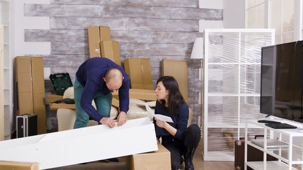 Caucasian young couple in new apartment assembling furniture and reading instructions. Boyfriend using screwdriver. Zoom in shot