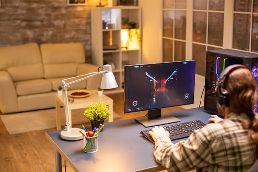 Back view of professional video gamer playing on powerful PC late at night in the living room.