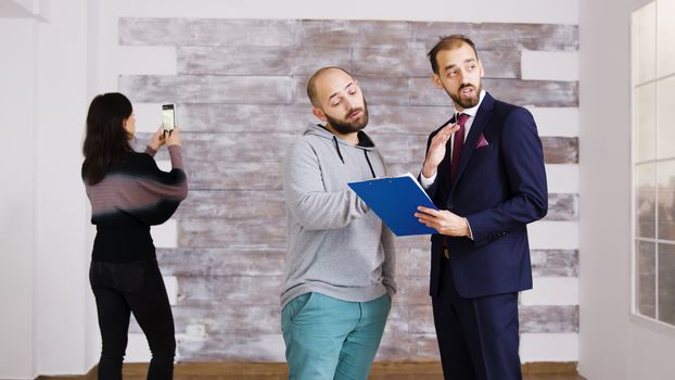 Real estate agent talking with client in empty apartment. Woman taking pictures in empty apartment.