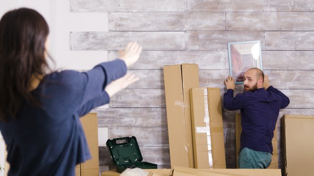 Caucasian couple hanging picture on the wall of new apartment. Couple decorating apartment.