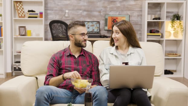 Young couple giving high five while sitting on the couch. Couplea enjoying soda and chips.