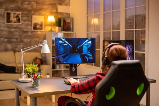 Back view of female gamer playing on powerful computer PC late at night in the living room.