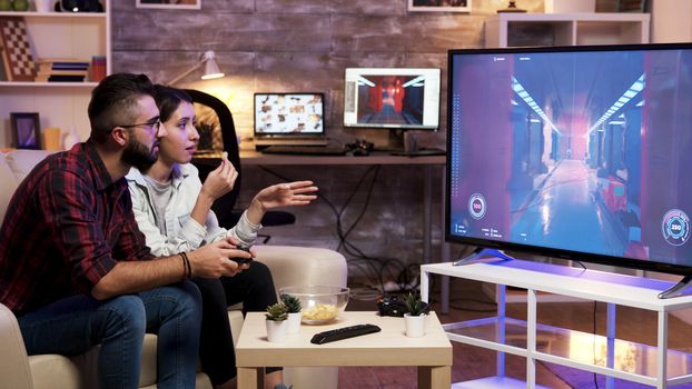 Man sitting on couch playing video games on television with girlfriend next to him.