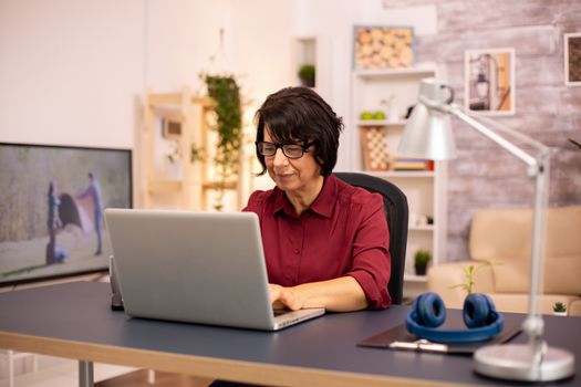 Old woman using a modern computer in her living room while her husband walks in the background