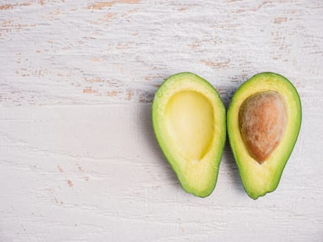 Avocado cut in half on white wooden board.