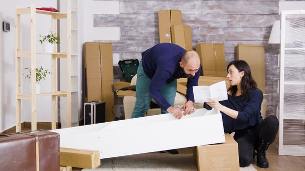Young couple assembling furniture as a team in new apartment. Girl reading assembly instructions.