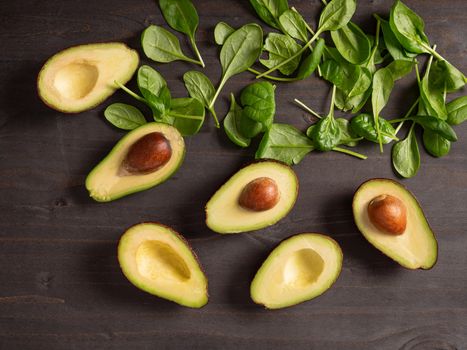 Top view of avocado next to baby spinach on dark wooden board